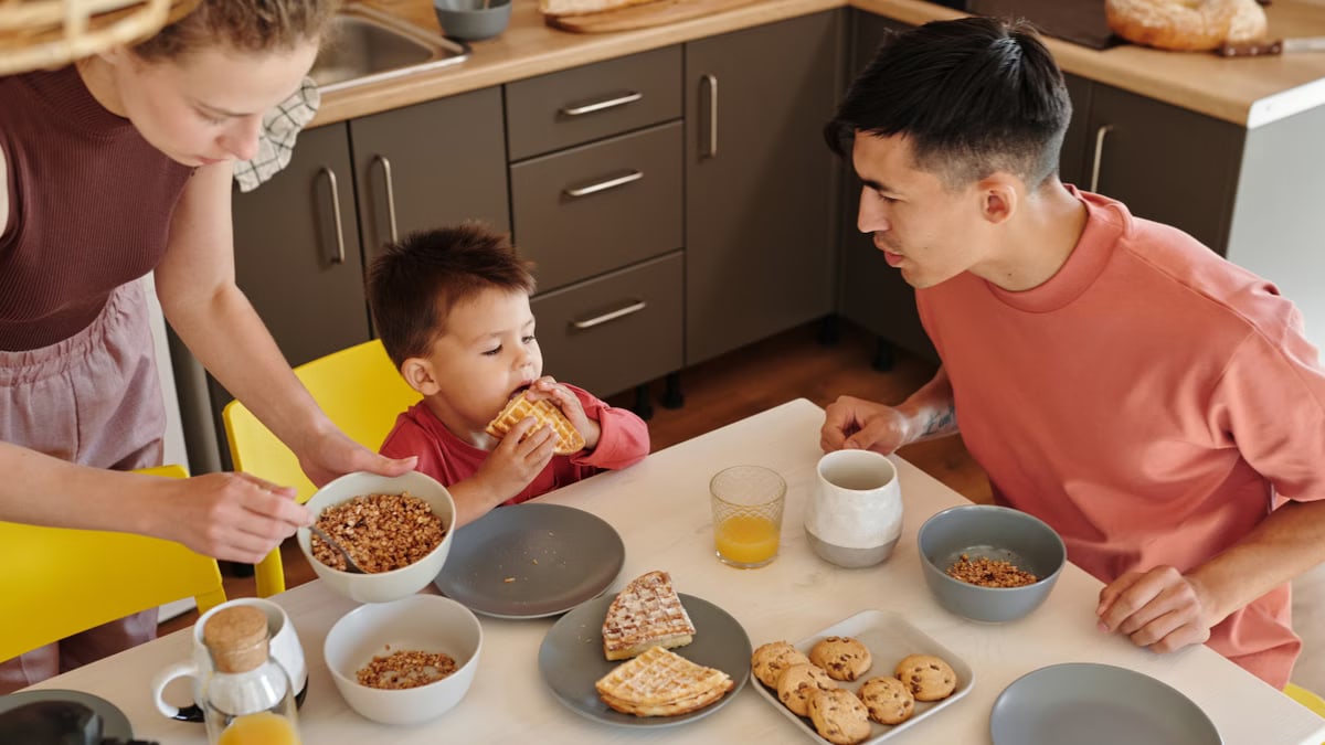 A joyful family of three sharing breakfast in a cozy kitchen setting, featuring waffles and cereal.